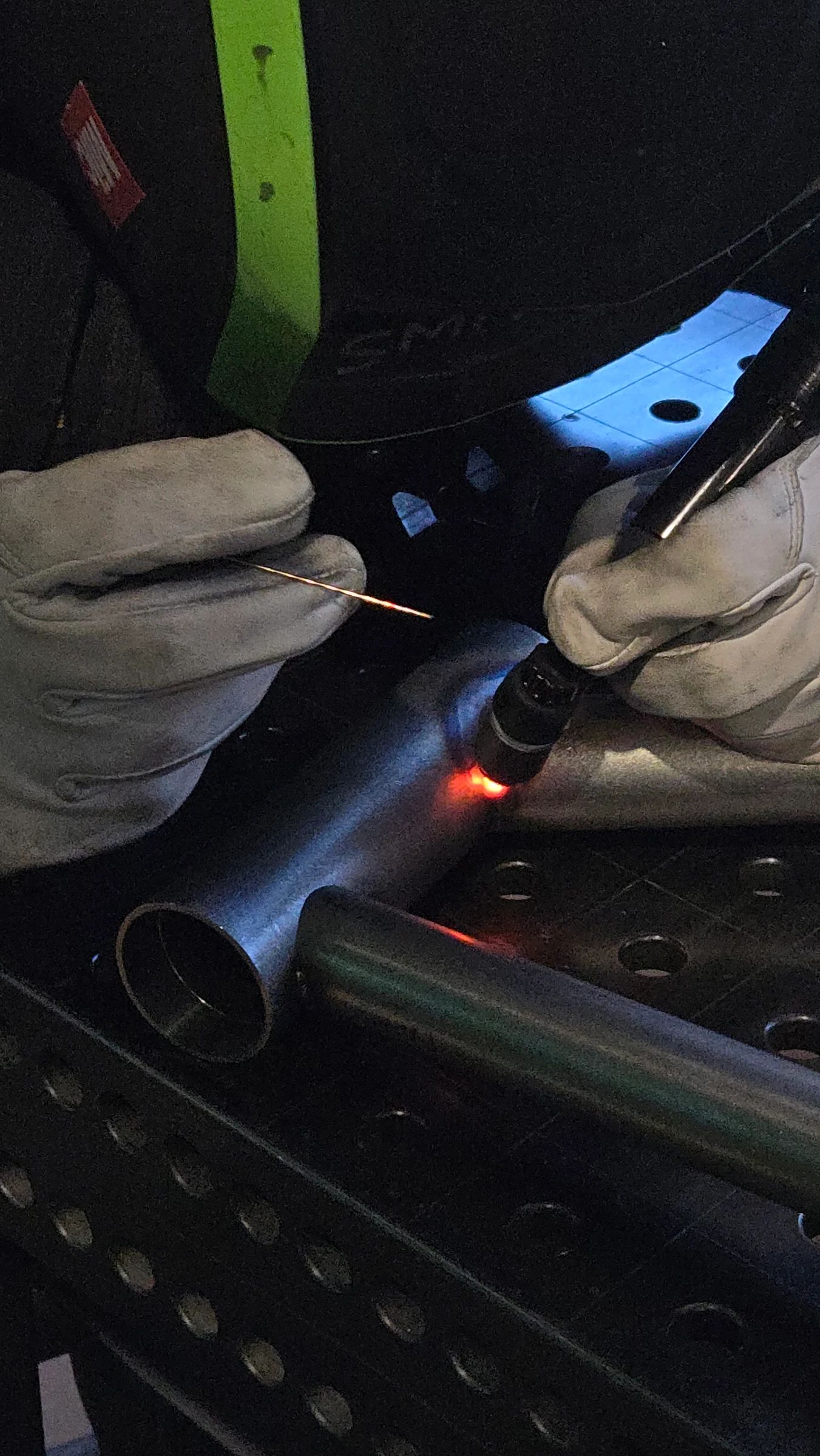 Soudure TIG en cours sur tube de cadre chromoly, mains gantées, torche à l'arc