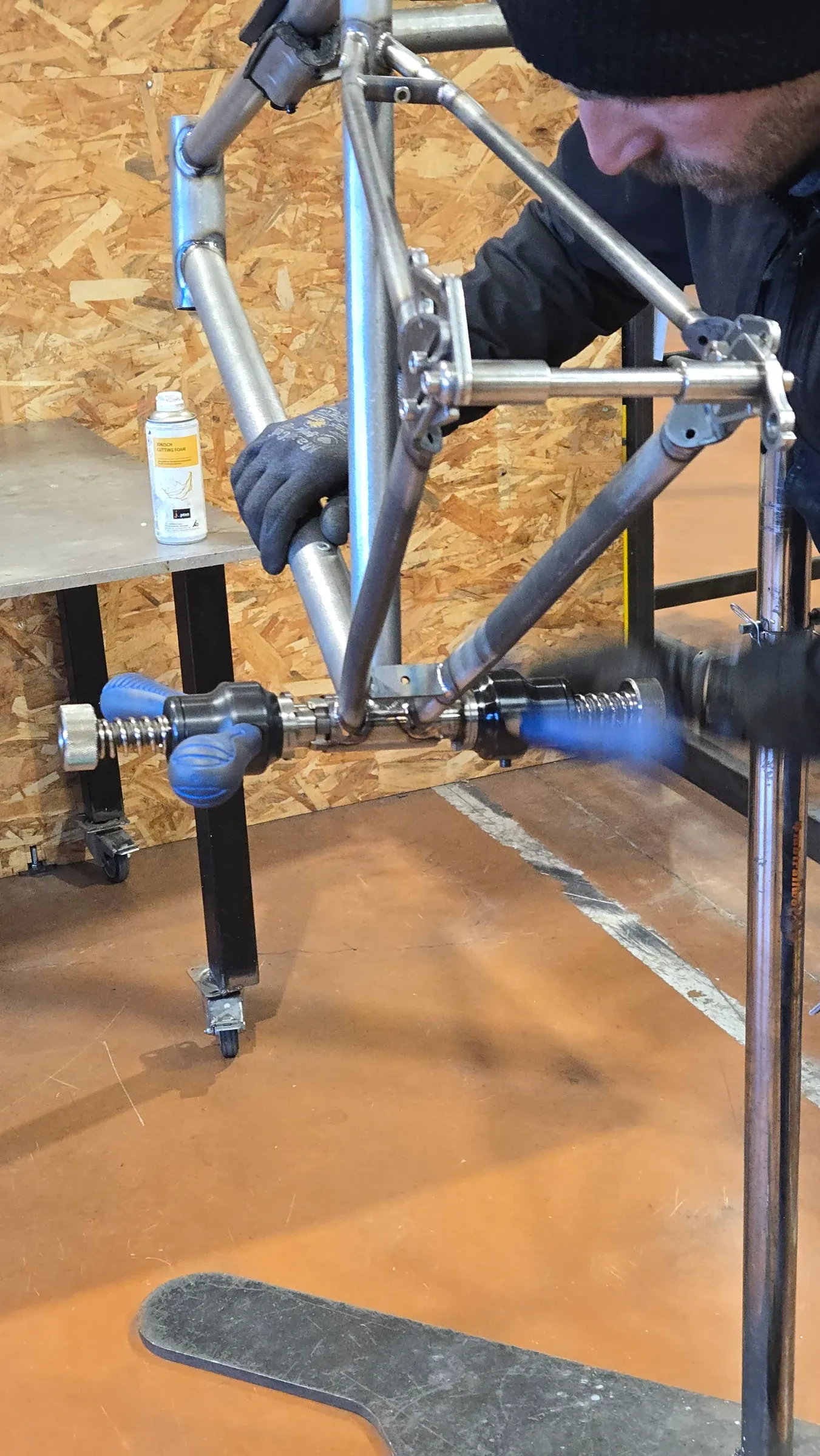 Surfaçage du boitier pédalier sur cadre chromoly en atelier, mains gantées, établi bois