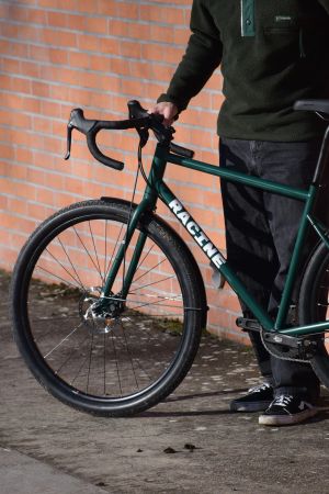 Détail du cintre drop bar du prototype Vélos-Racine vert mousse, main posée sur le guidon, fond de mur en brique